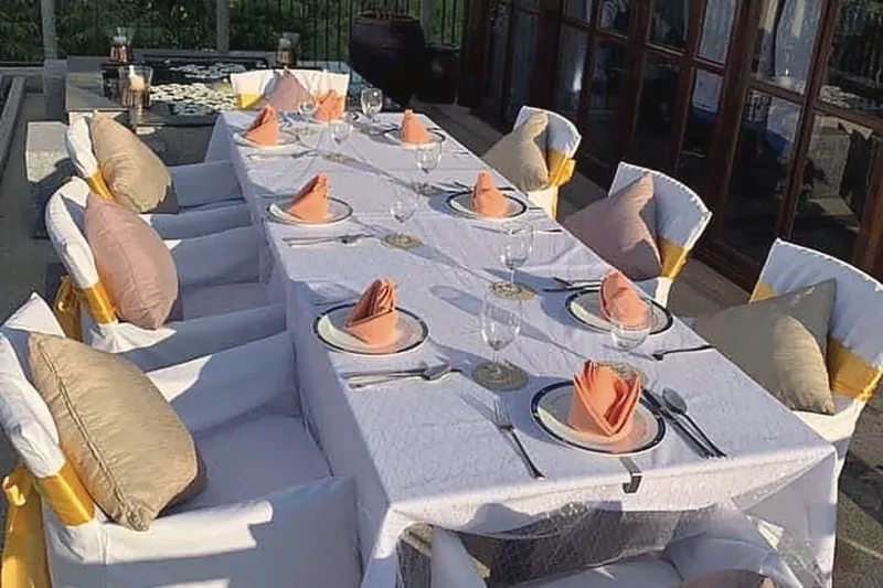 A long table on the deck dressed for a wedding dinner, white chair covers with gold sashes